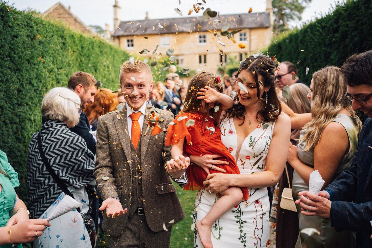 Wedding guests gather outdoors at a garden celebration on a sunny day.