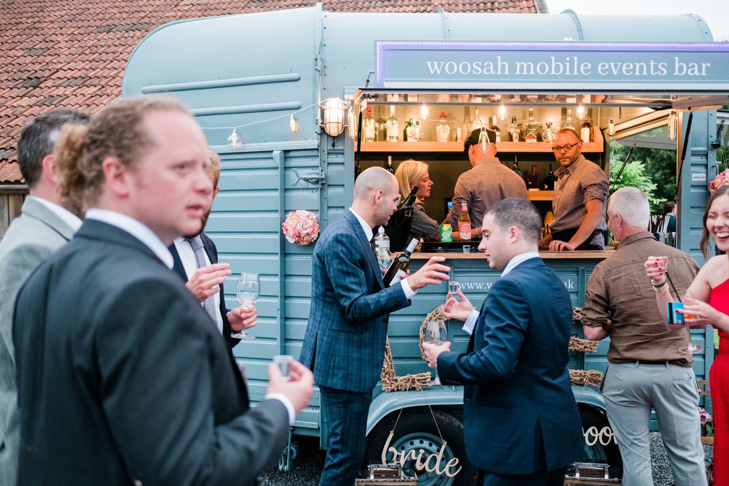 Wedding guests in formal attire socializing outside blue-painted venue wall.