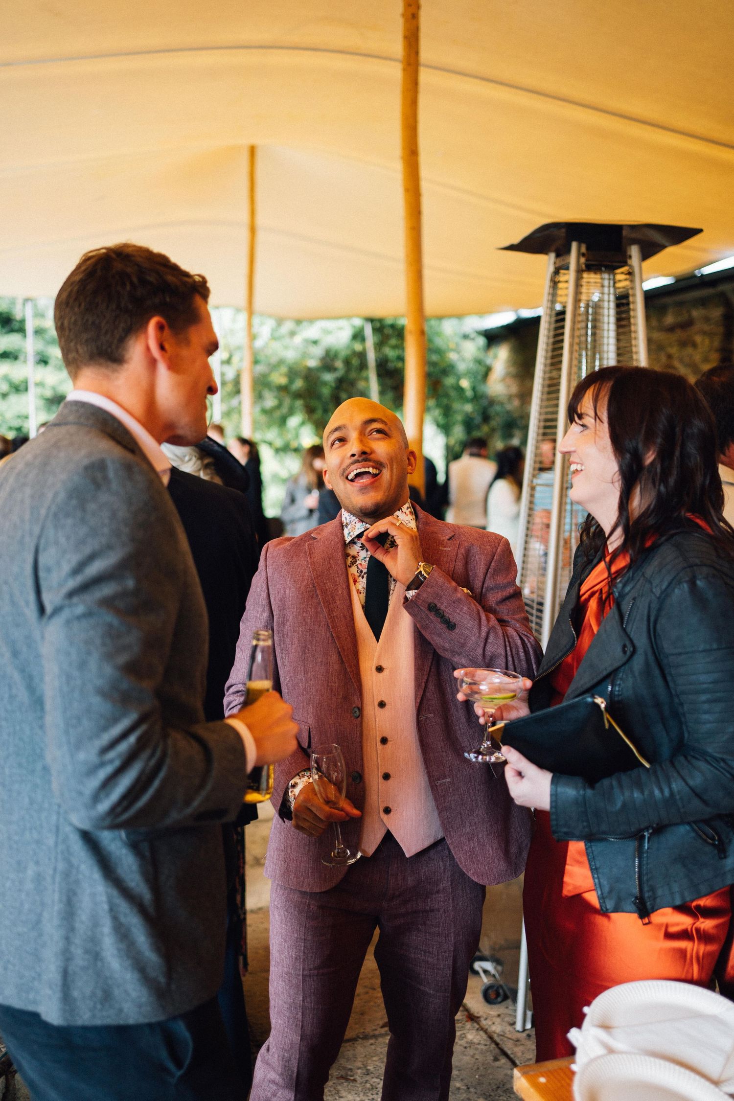 Wedding guests mingle and socialize under a warm-lit tent during an outdoor reception celebration.