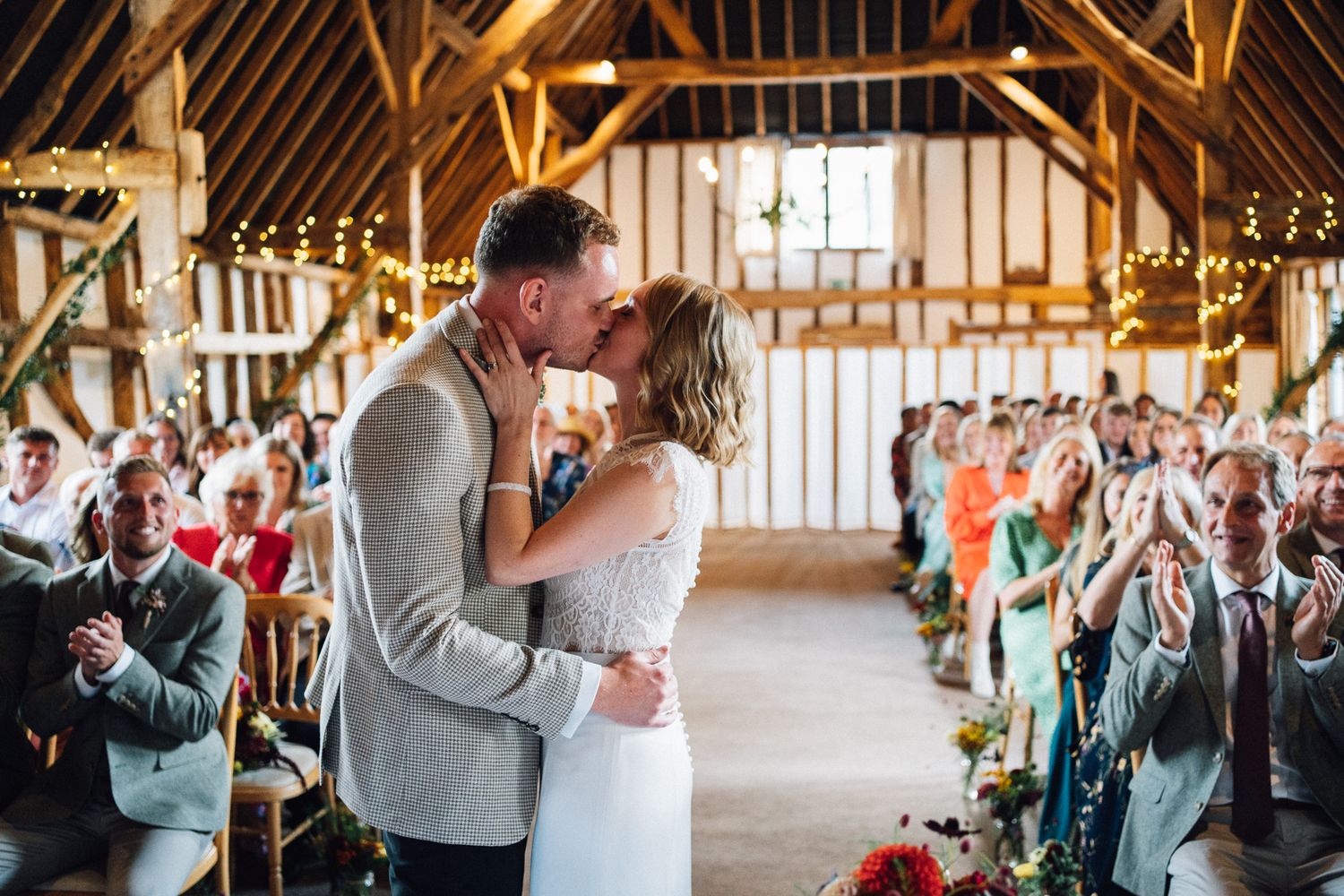 Wedding guests celebrating and cheering during a ceremony in a rustic wooden barn venue.