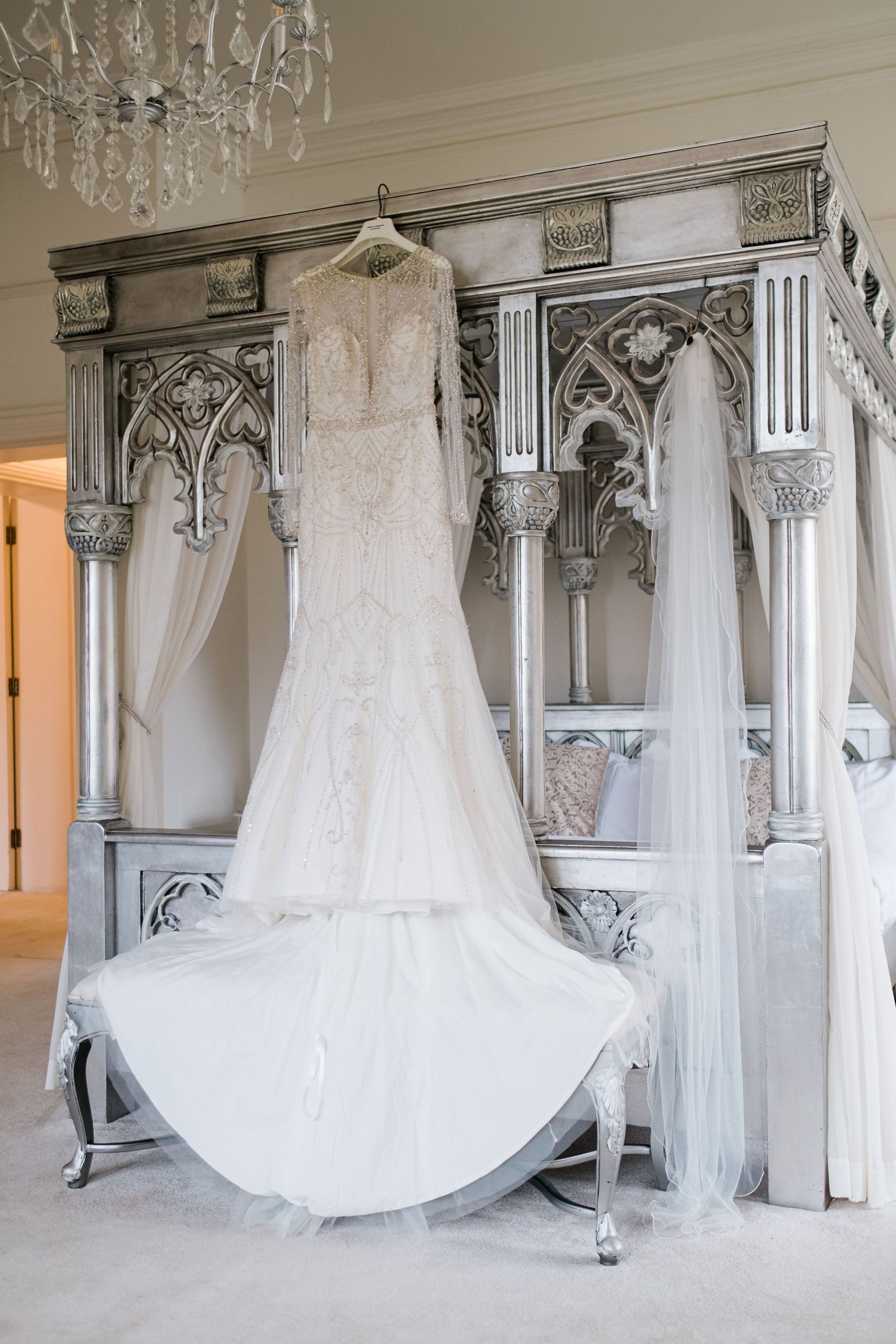 An elegant white wedding gown displayed on an ornate Gothic-style wardrobe under a crystal chandelier.