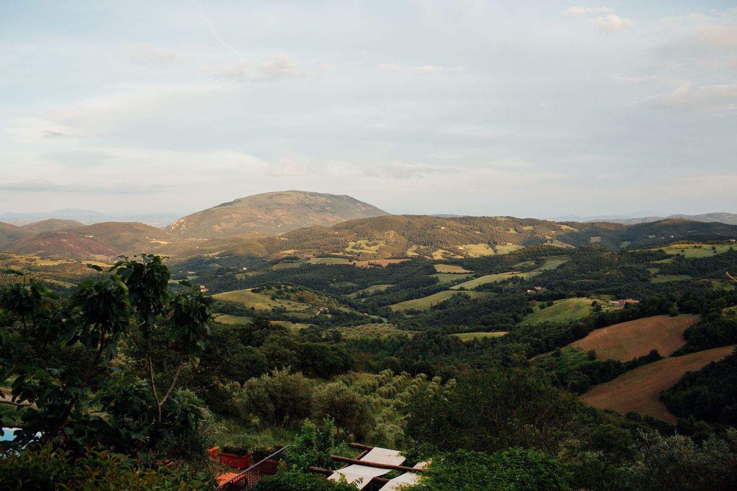 Panoramic view of rolling hills and countryside landscape under a cloudy sky.