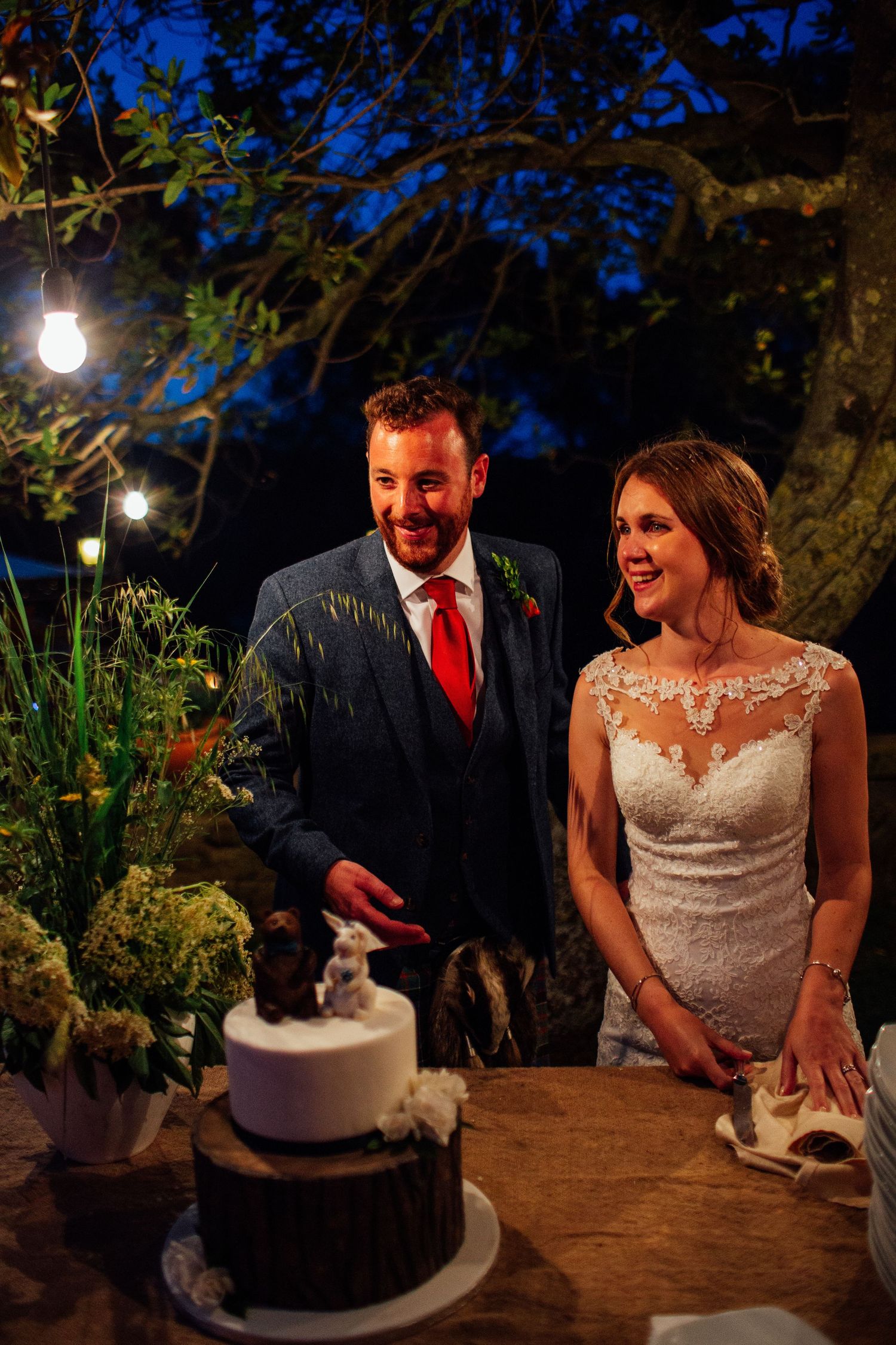 A couple cuts their wedding cake during an evening outdoor reception.