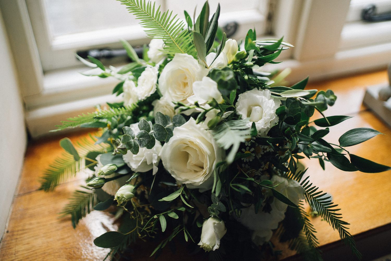 Elegant white rose and greenery wedding bouquet arrangement displayed on wooden surface.