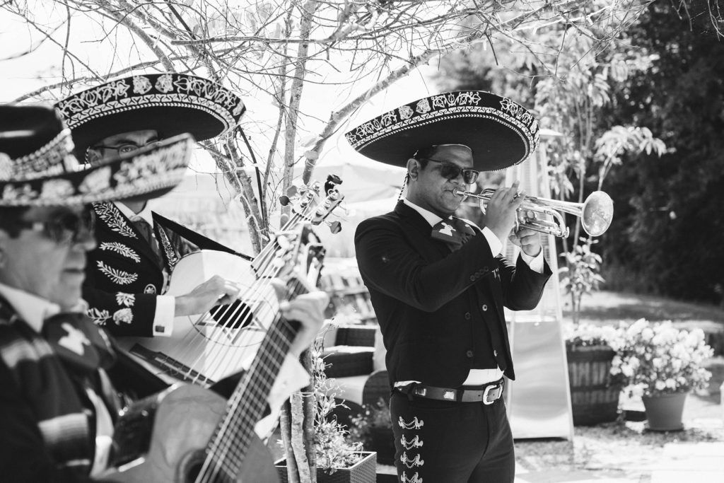 Black and white photo of mariachi band members playing instruments while wearing traditional sombreros.