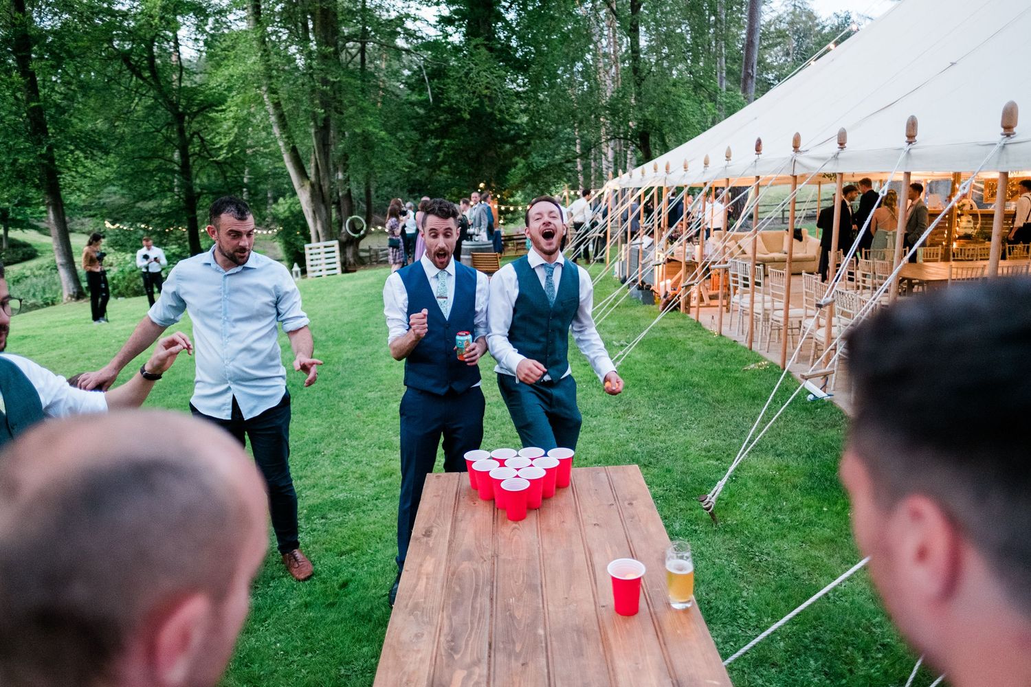 Wedding guests enjoy outdoor games and entertainment near rustic wooden benches.