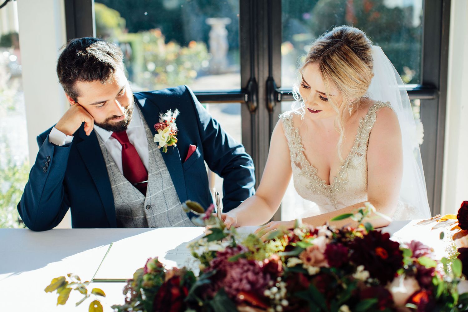 Wedding ceremony progresses with decorative floral arrangements on tables in foreground.