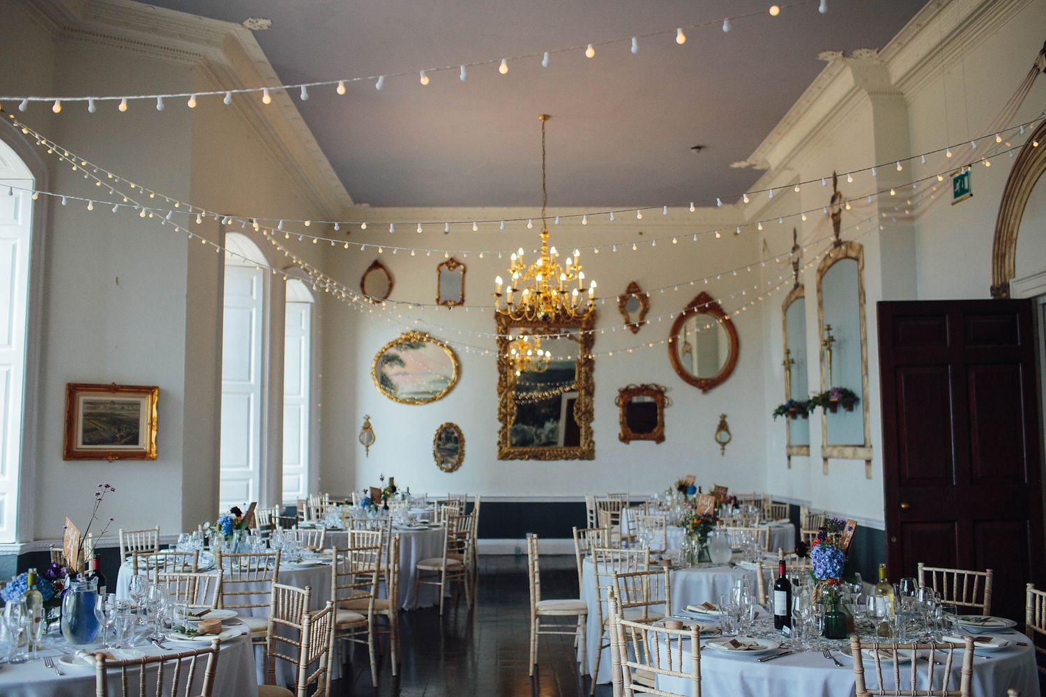 Elegant reception room with string lights, mirrors and table settings for wedding celebration.