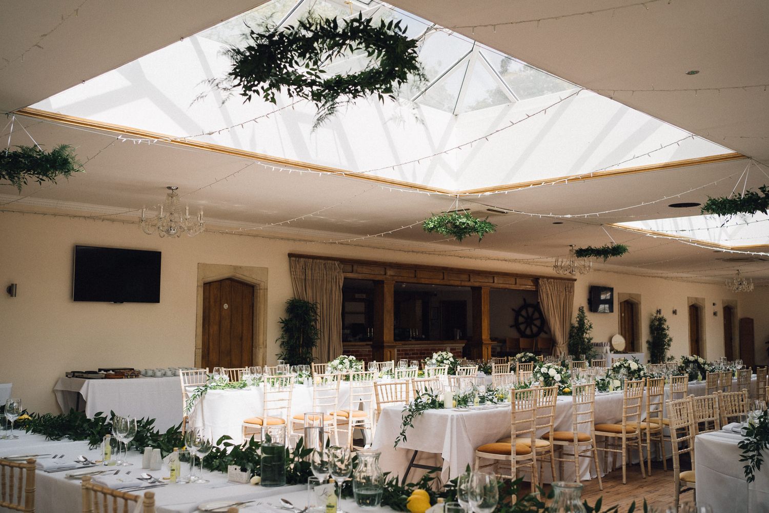 Spacious wedding reception hall decorated with hanging greenery and natural skylights.