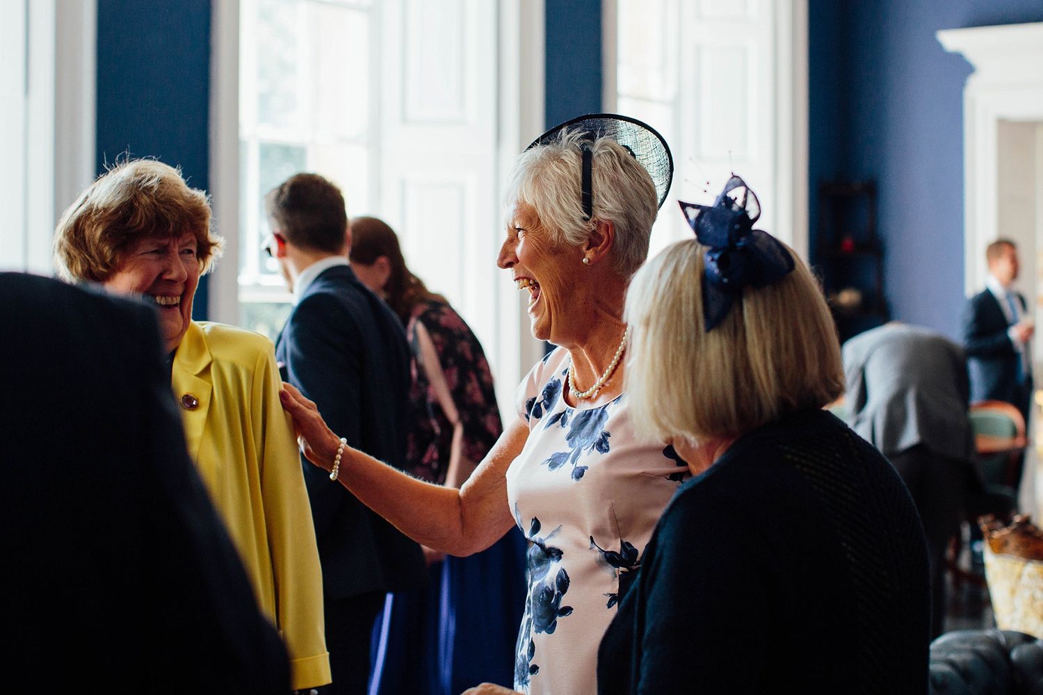 Wedding guests mingle in a sophisticated venue with deep blue walls and white trim.