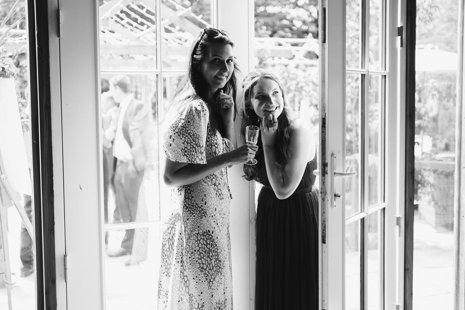 Wedding guests gather in a bright indoor venue with large windows and natural light.