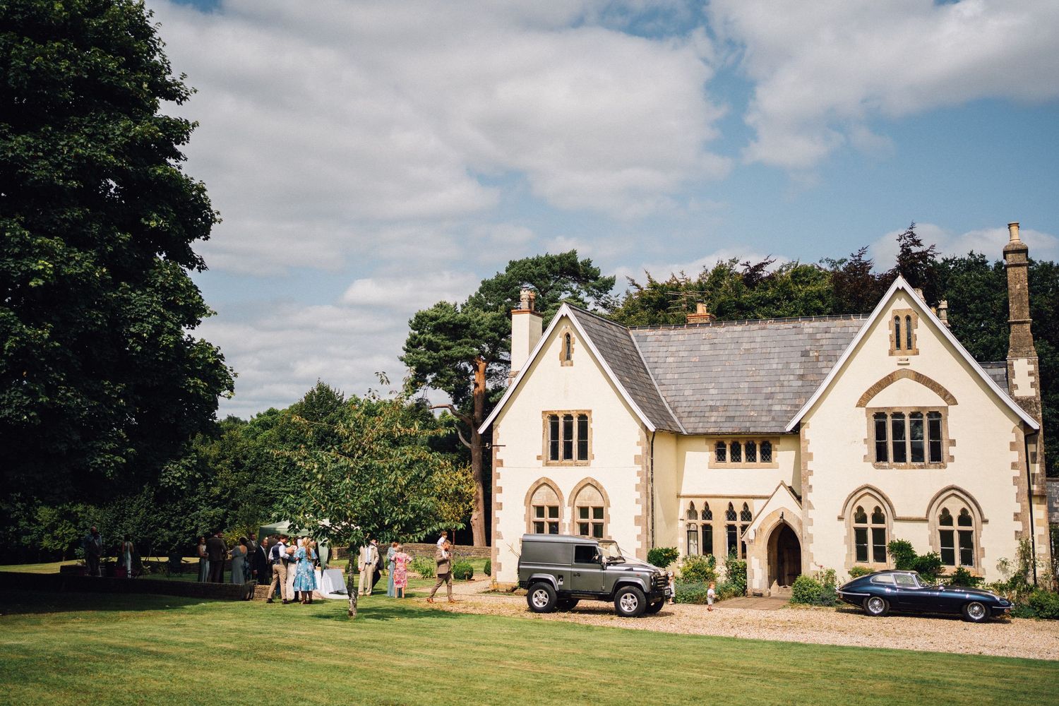 Panoramic view of a classic Gothic Revival style stone wedding venue with multiple buildings under cloudy skies.