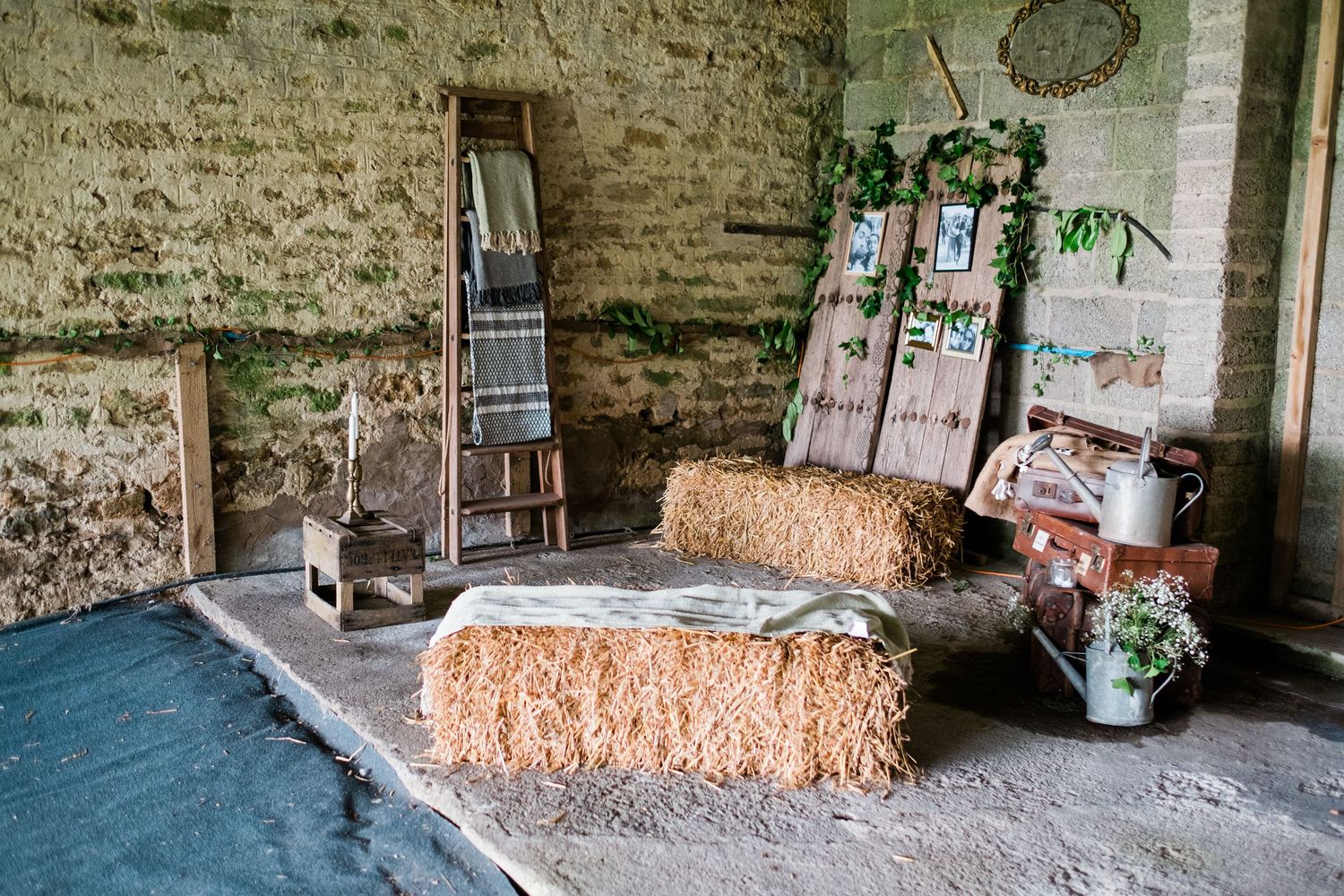 Rustic barn interior with exposed stone walls and straw bales arranged in a corner.
