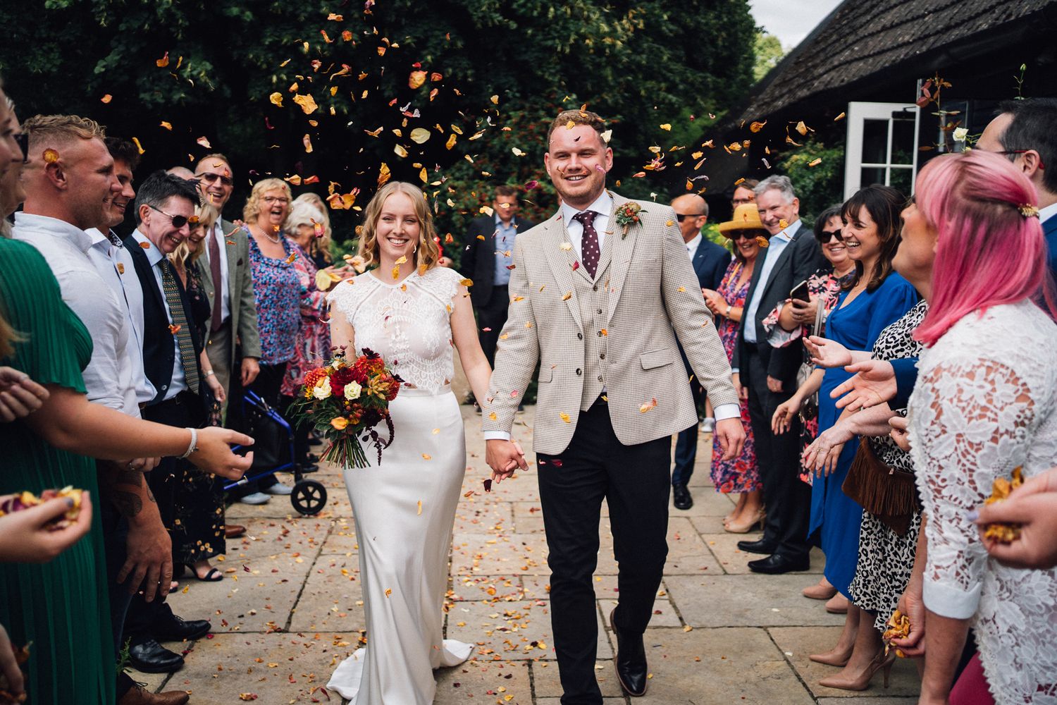 Wedding party and guests throwing confetti during an outdoor celebration.