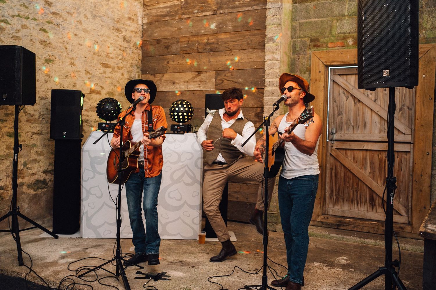 Band performs live music at rustic barn wedding venue with wooden backdrop.