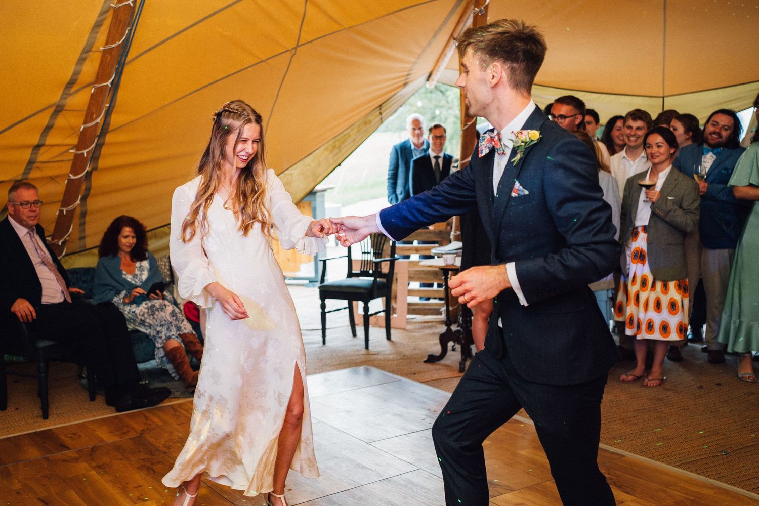 Wedding celebration with dancing and festivities under a yellow tent.