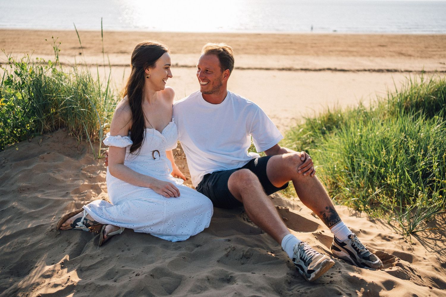 Couple sharing intimate moments while relaxing on beach sand during golden hour.