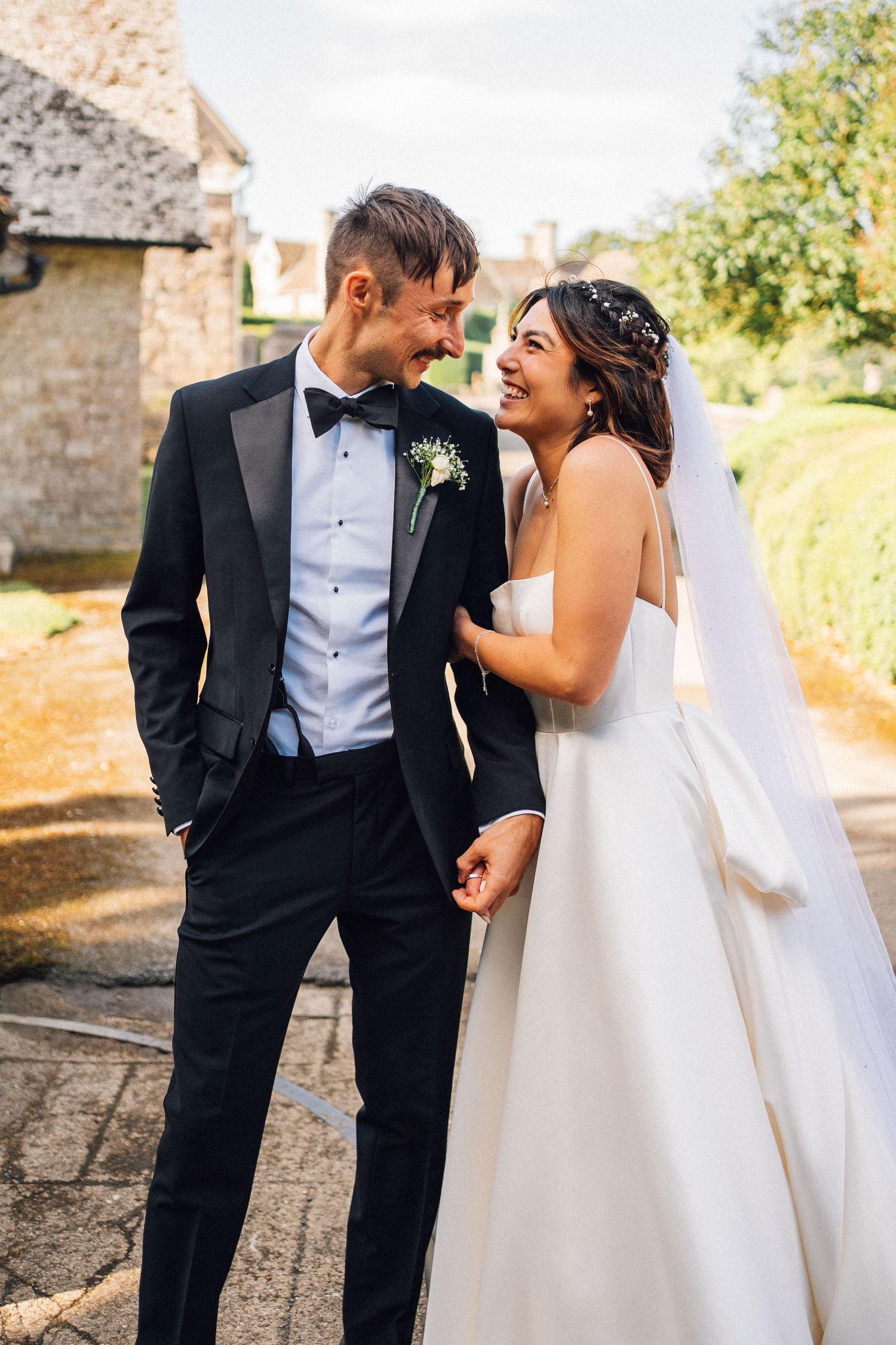 A couple shares joyful moments in formal wedding attire against a stone wall backdrop.
