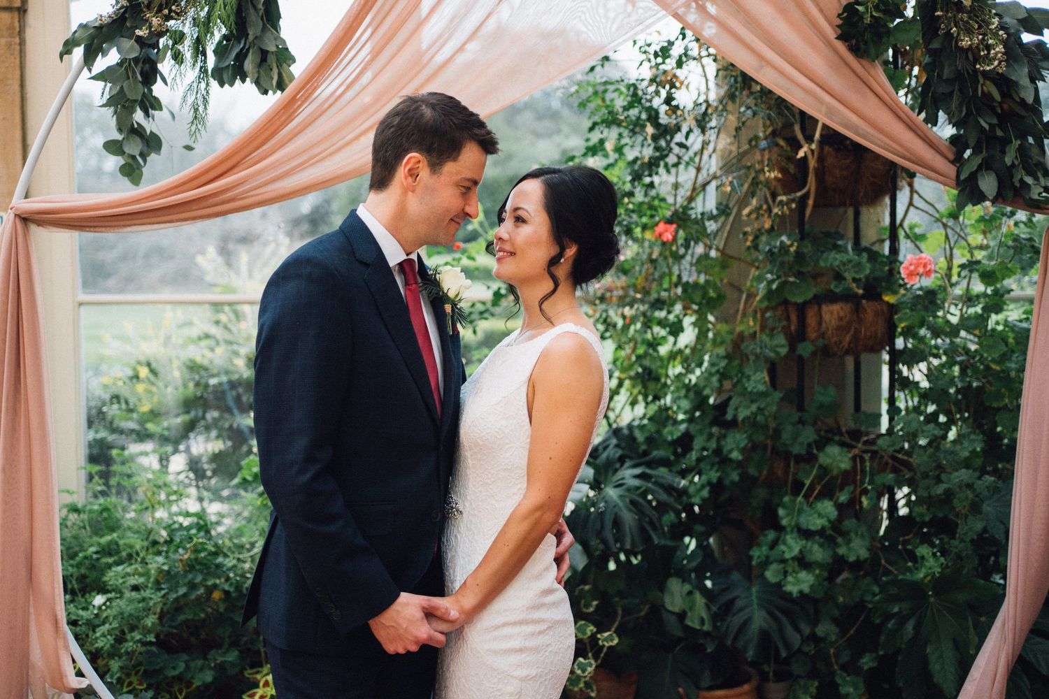 Romantic wedding ceremony setup with blush pink drapes and floral arrangements in an outdoor garden setting.