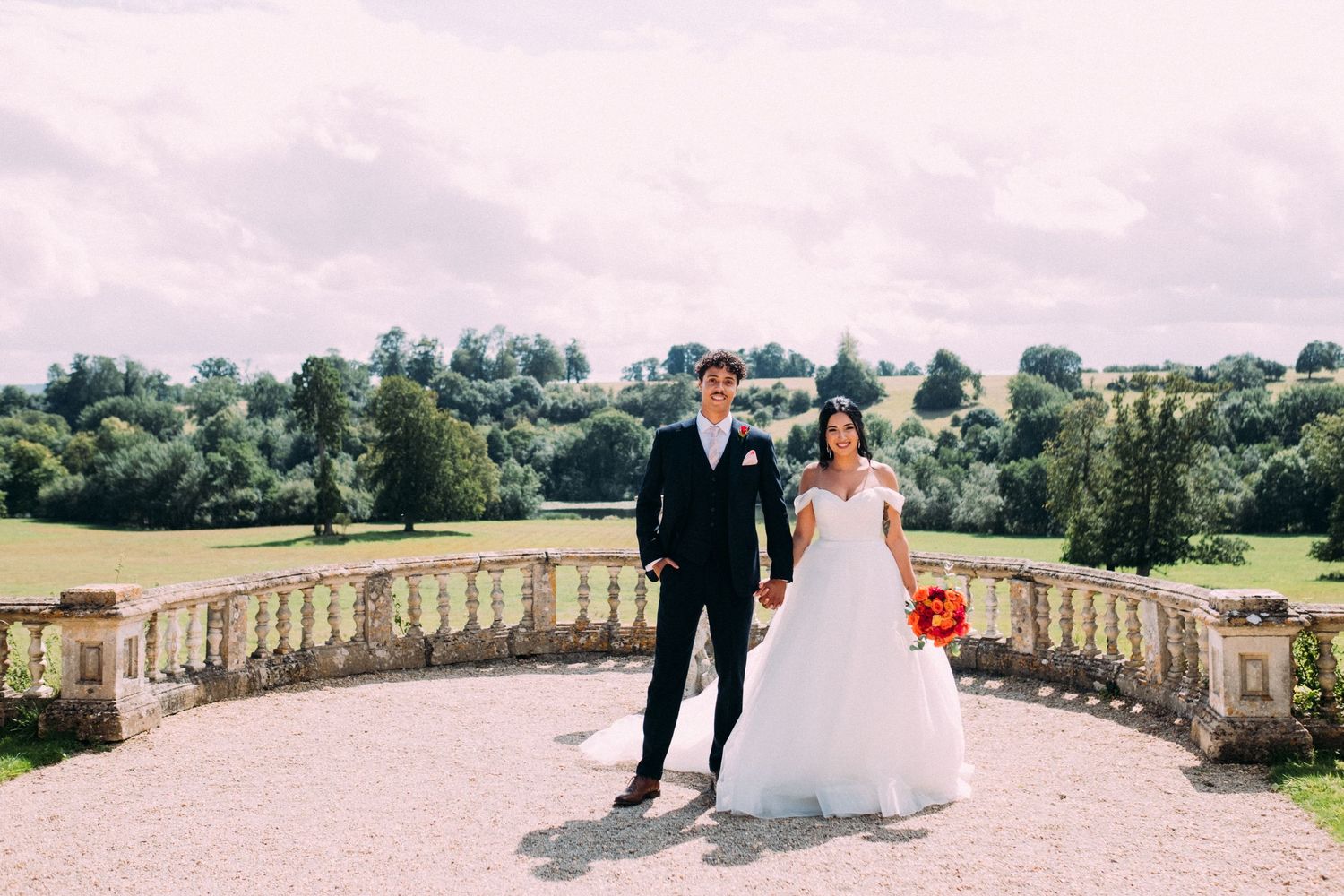 Newlyweds walking along a stone balustrade at an elegant estate.