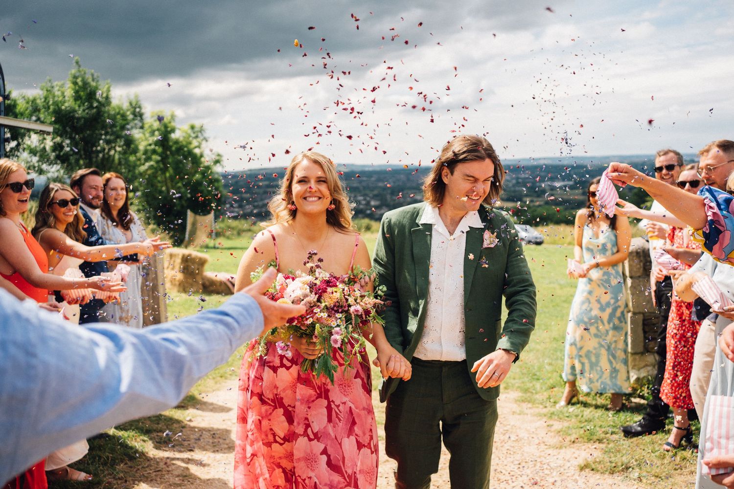 Wedding guests throw pink flower petals during an outdoor celebration.
