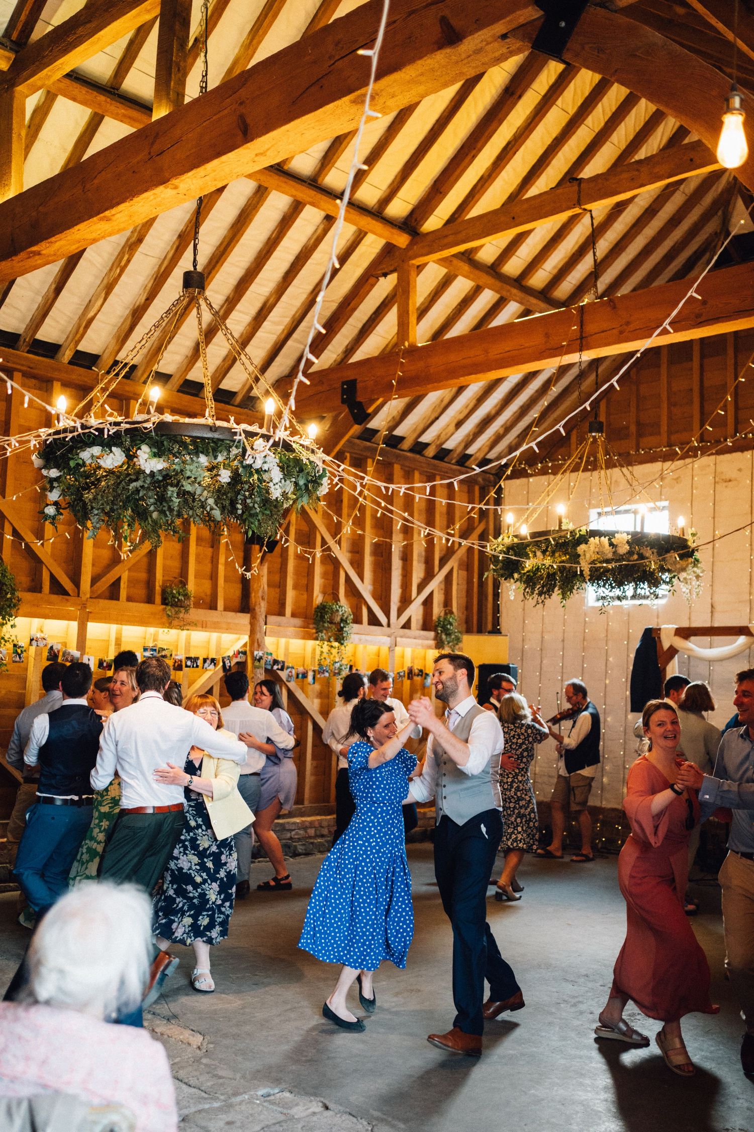 Panoramic view of couples dancing in a rustic wooden barn with exposed beams and festive decorations.