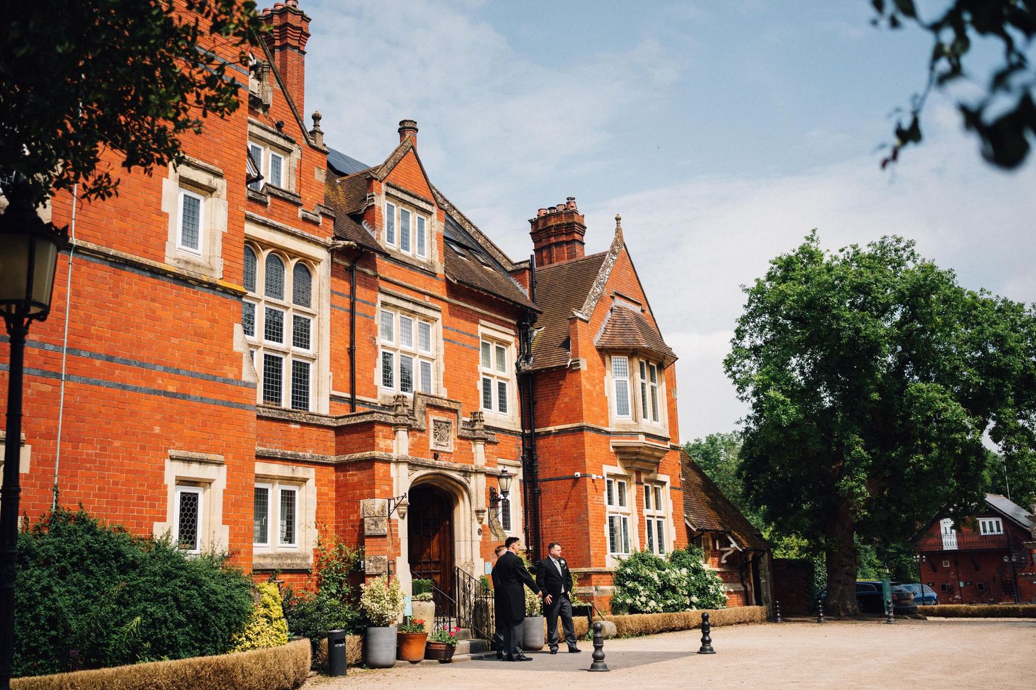 Grand Victorian red brick manor house wedding venue with manicured grounds and elegant architecture on a sunny day.