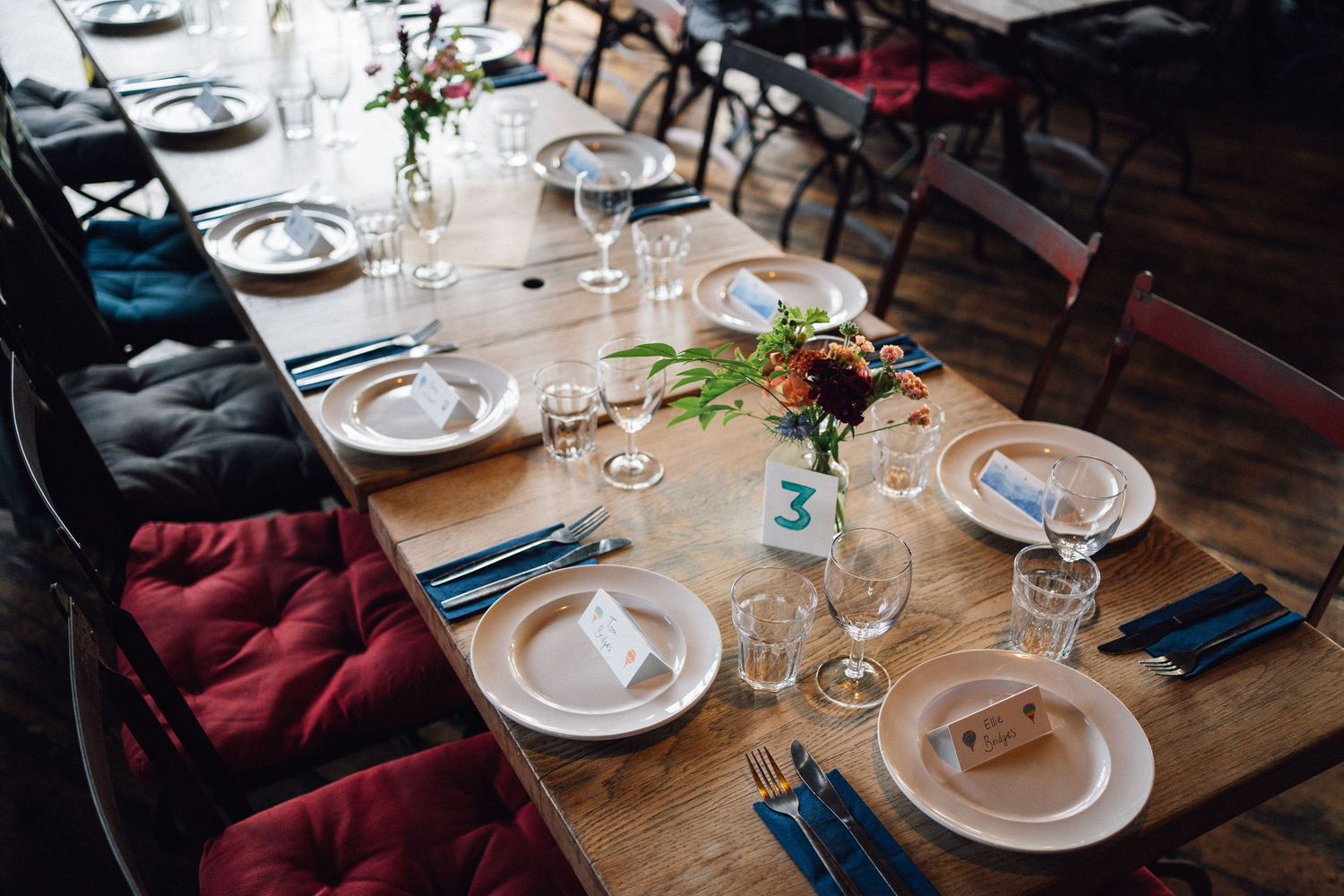 Rustic wooden dining tables set for wedding reception with wine glasses and place settings.