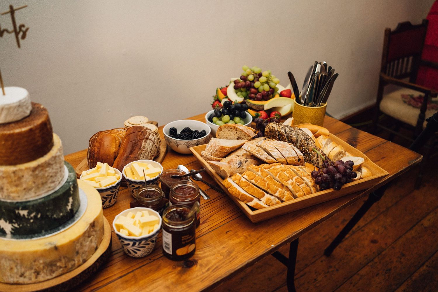 A wooden table displays an assortment of breakfast pastries, fruits, and beverages in a cozy home setting.