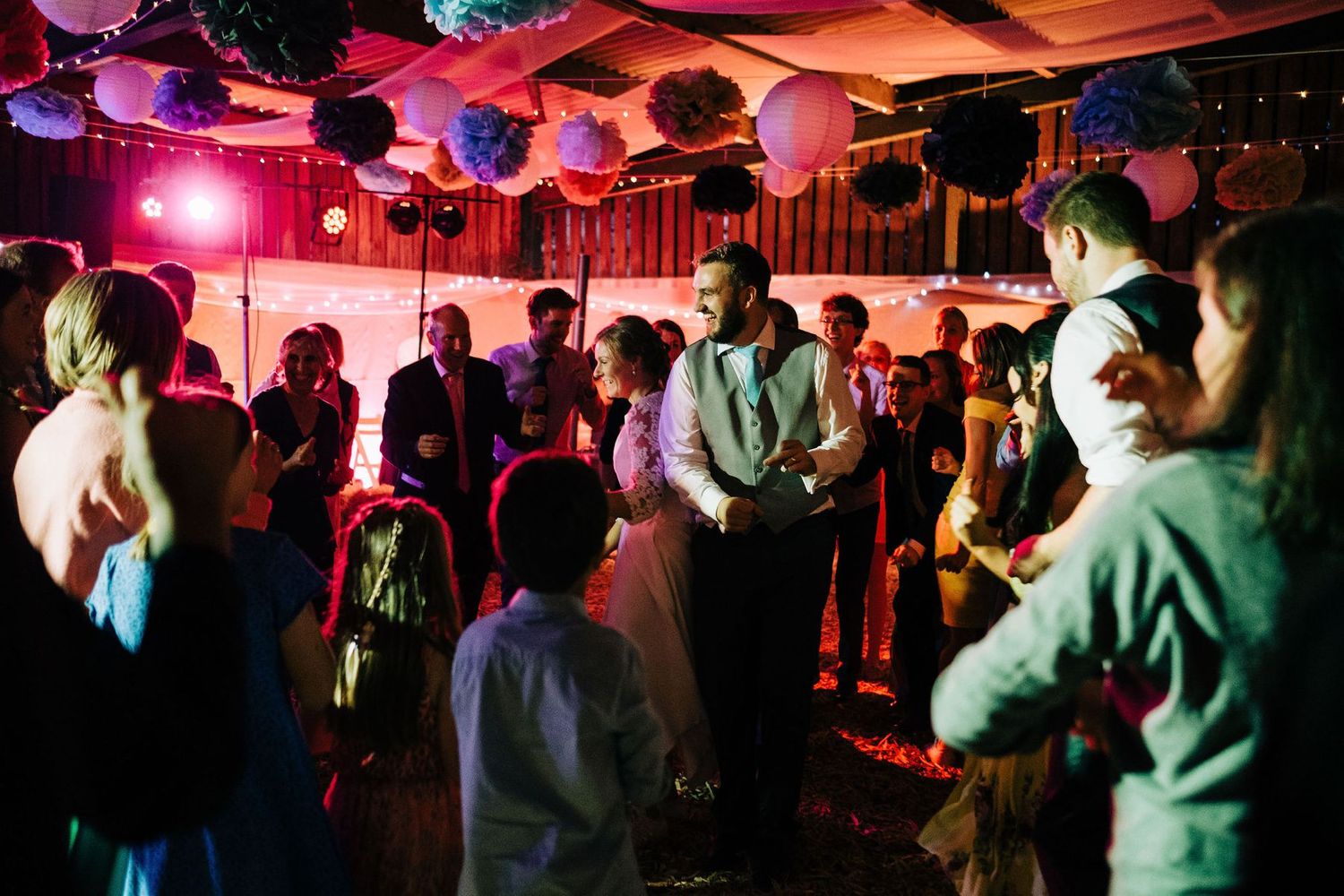 Dimly lit dance floor with red lighting and party guests dancing at a wedding reception.