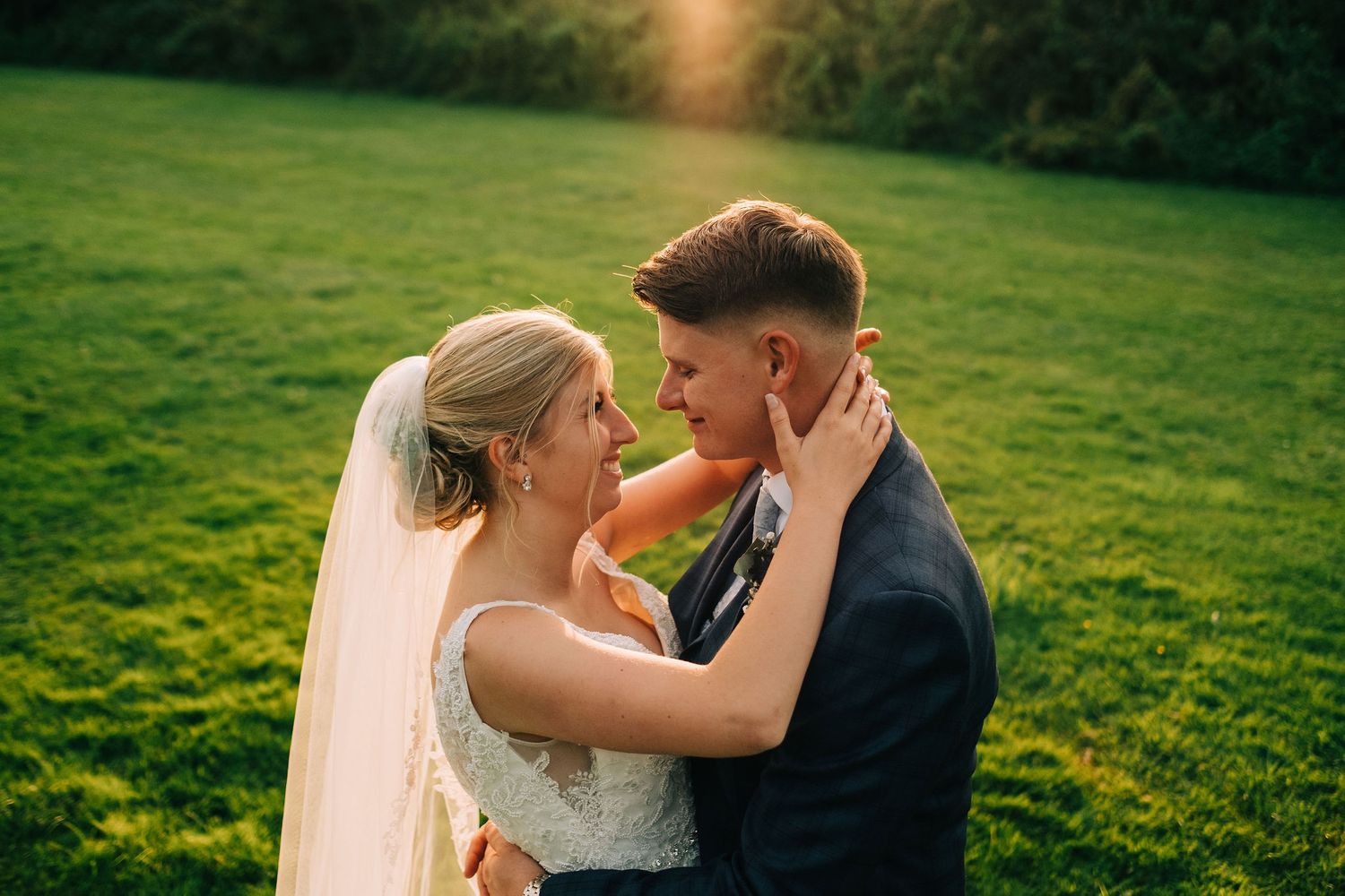 Wedding couple embracing in a grassy field during golden hour photography session.