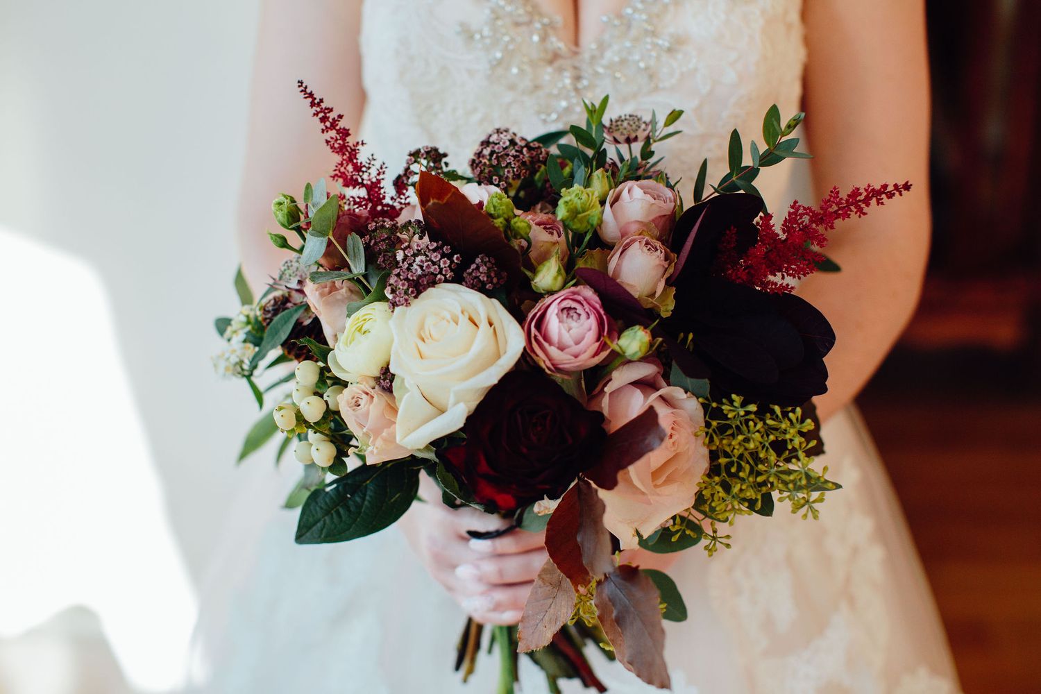 Romantic wedding bouquet featuring pink roses, burgundy flowers and greenery.