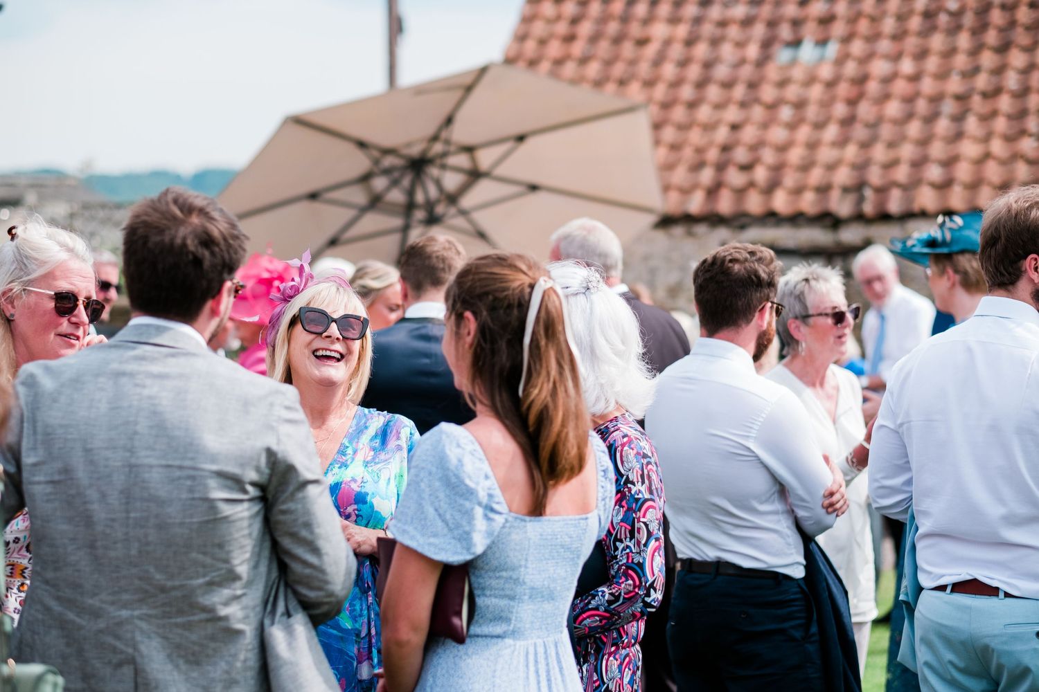 Guests mingle at an outdoor summer party under a terracotta-roofed building.