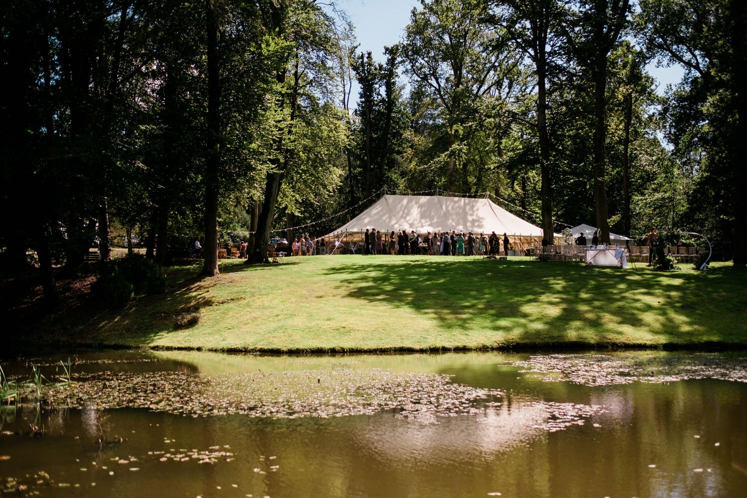 Panoramic view of a lakeside wedding venue with white tent and natural landscaping.