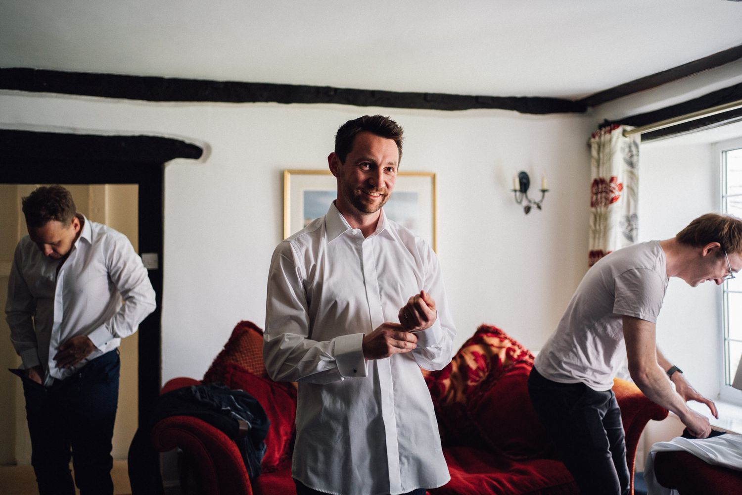 Men getting dressed in formal attire in a bright white room.