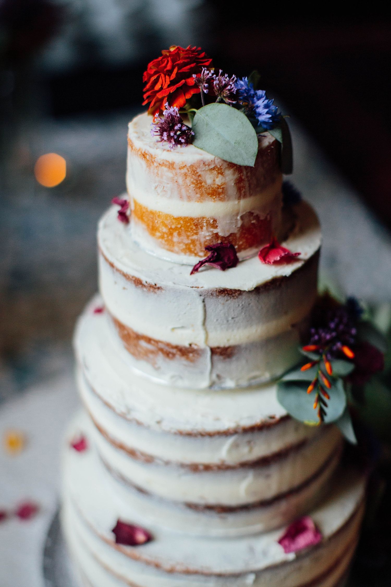 Multi-tiered naked wedding cake decorated with fresh berries and flowers.