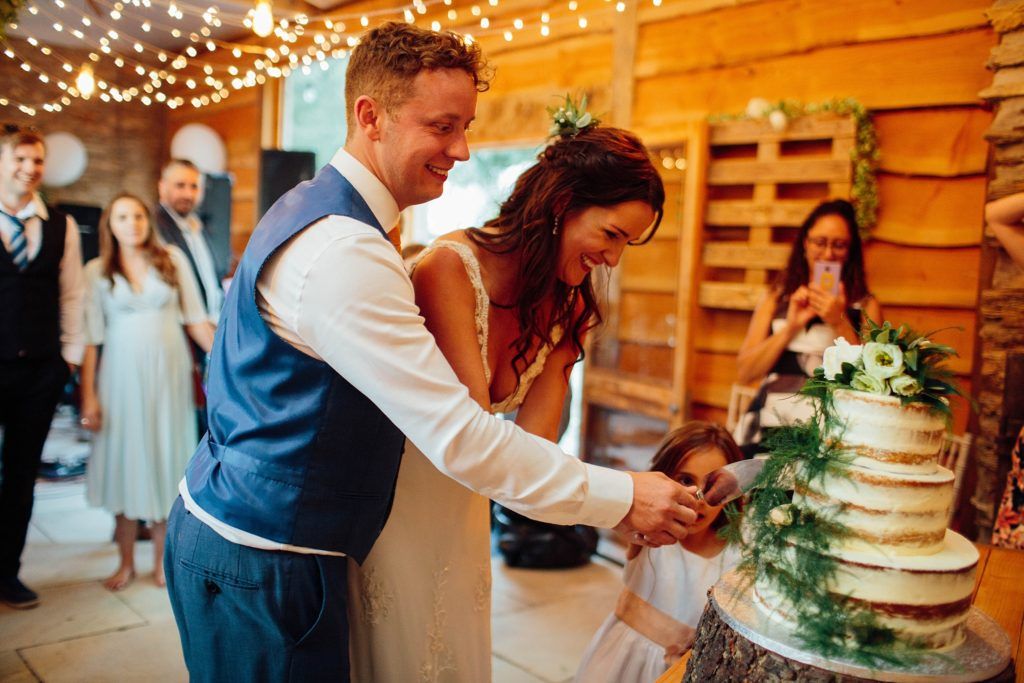 Rustic barn wedding reception with string lights and elegant cake cutting moment.