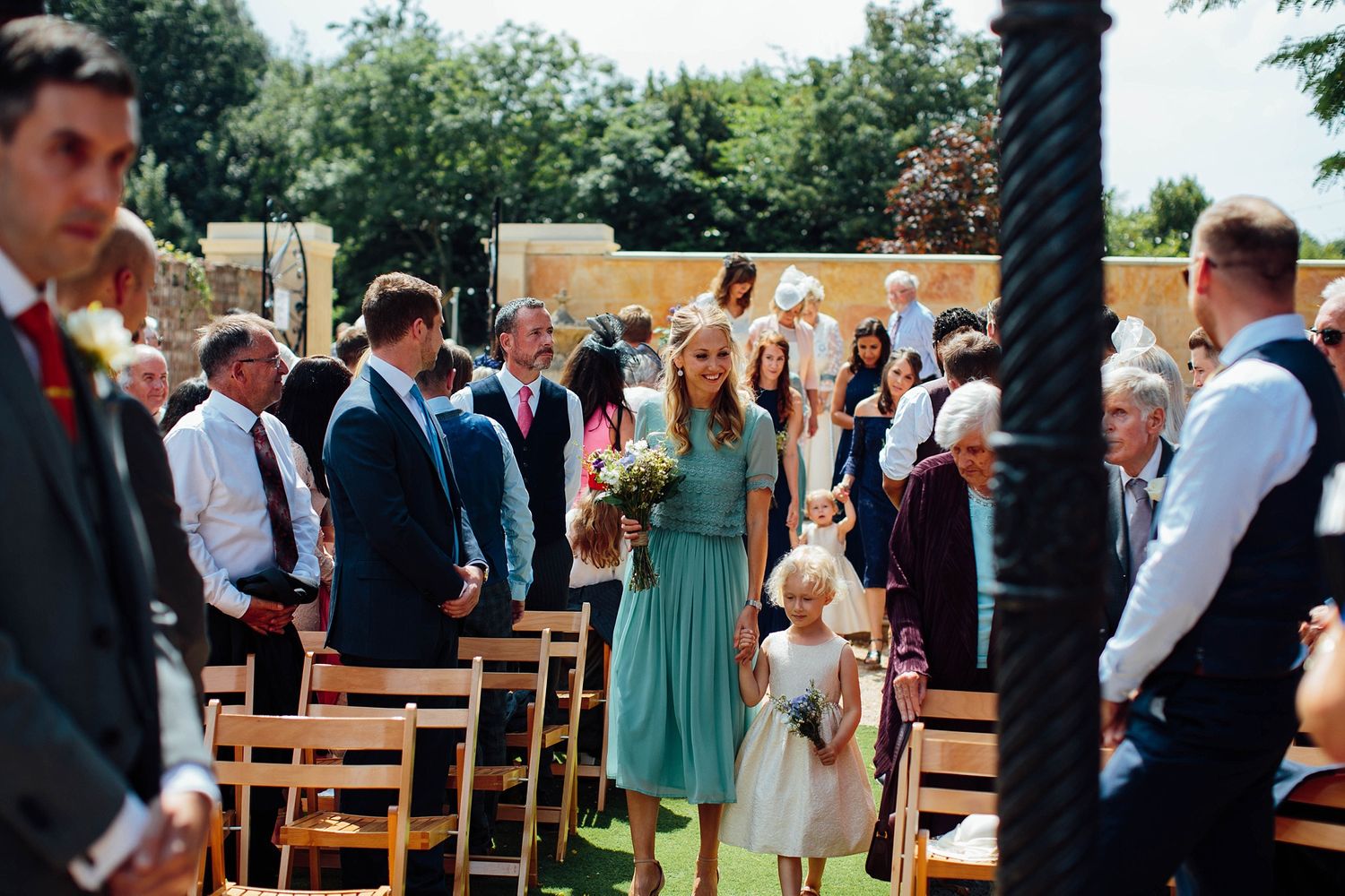 Wedding ceremony guests gathered under a covered outdoor venue with brick walls.