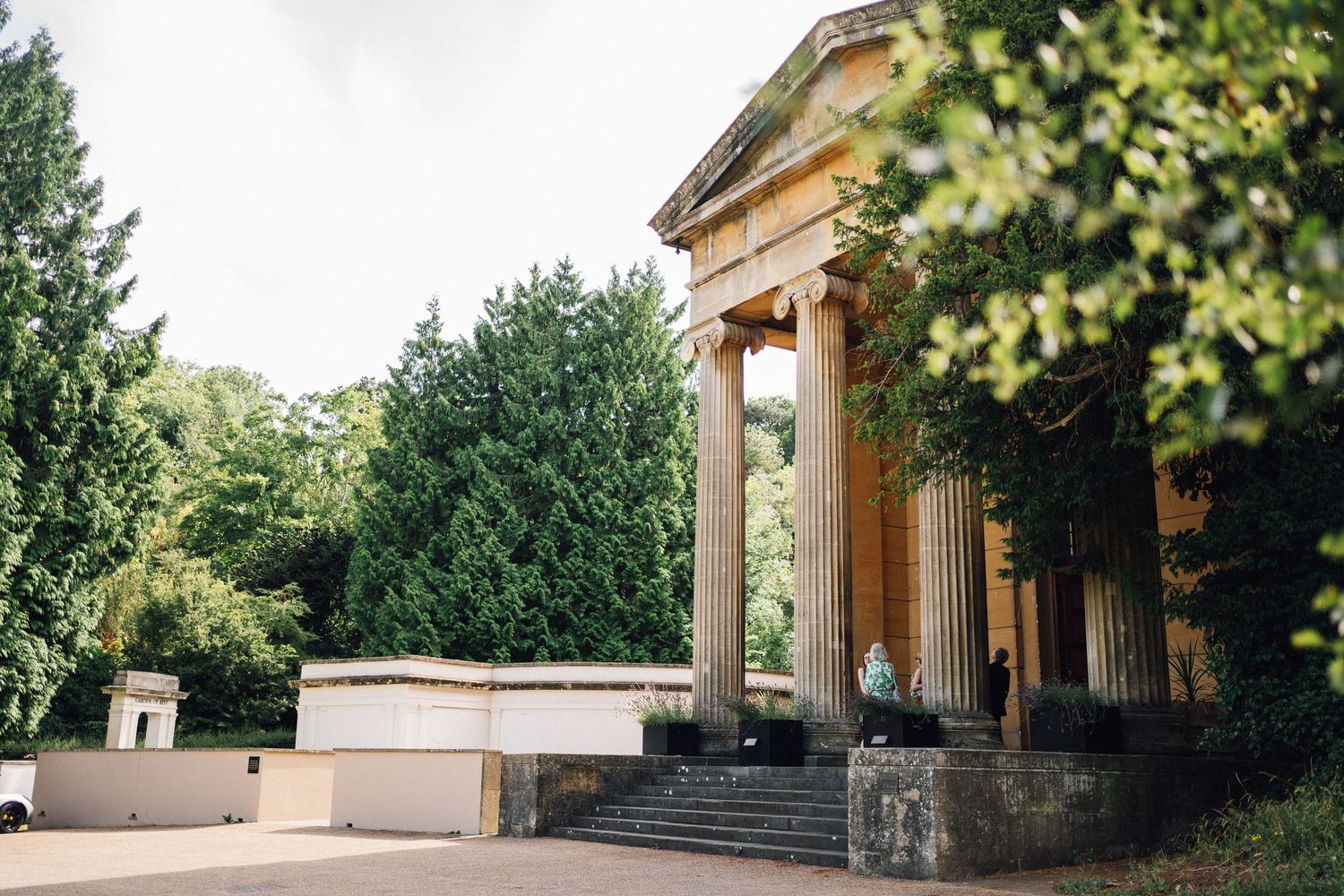 Classical stone colonnade building with steps surrounded by lush greenery.