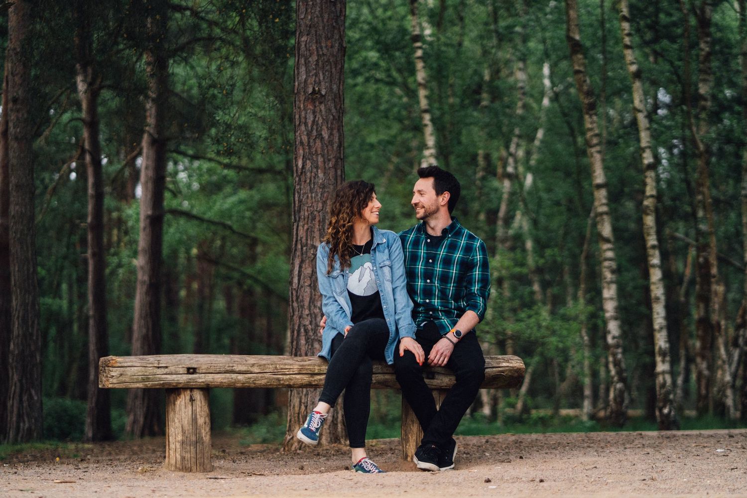 A couple sits together on a wooden bench in a serene forest setting.