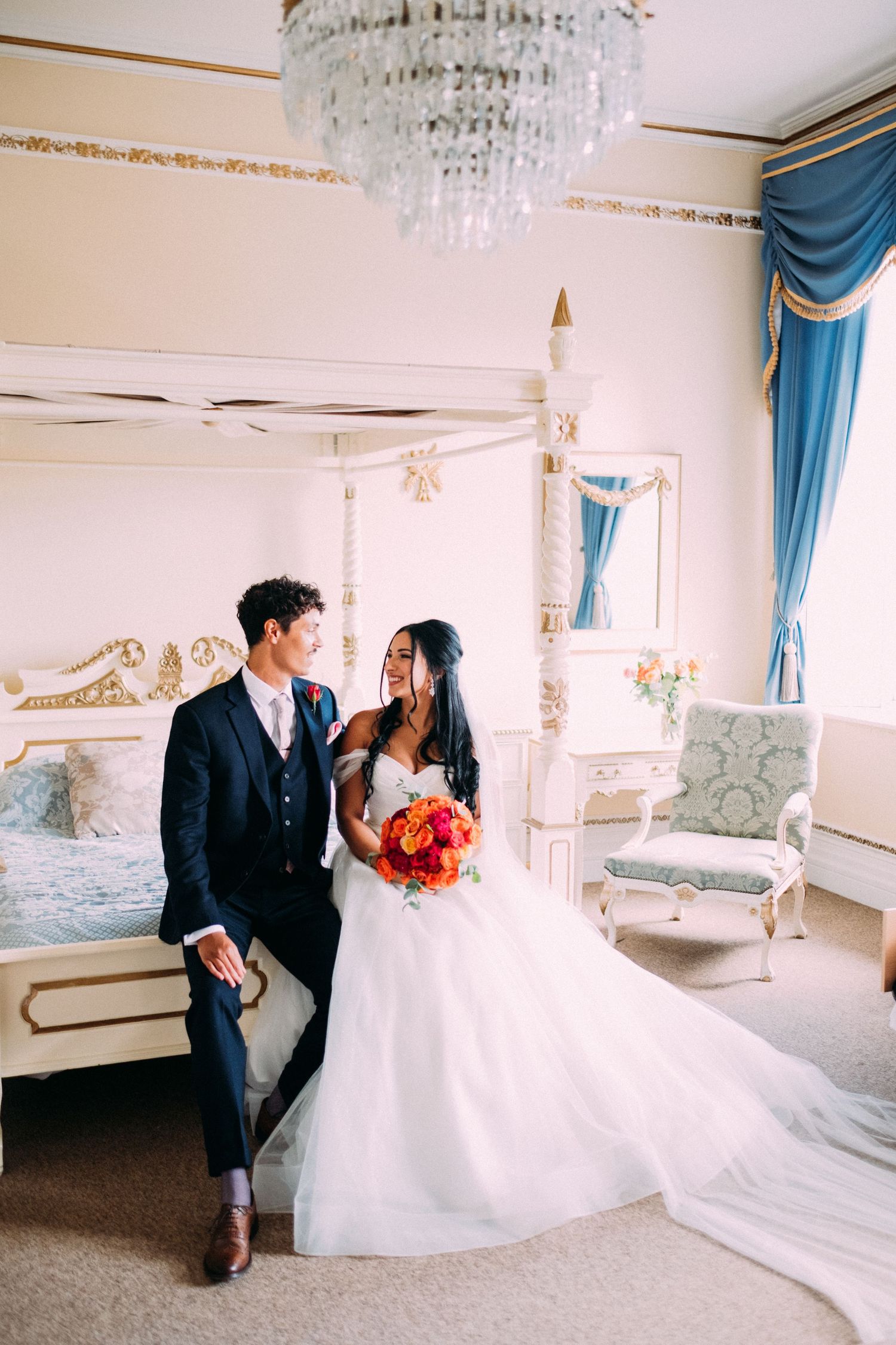 Elegant white room with crystal chandelier and blue curtains featuring wedding couple.