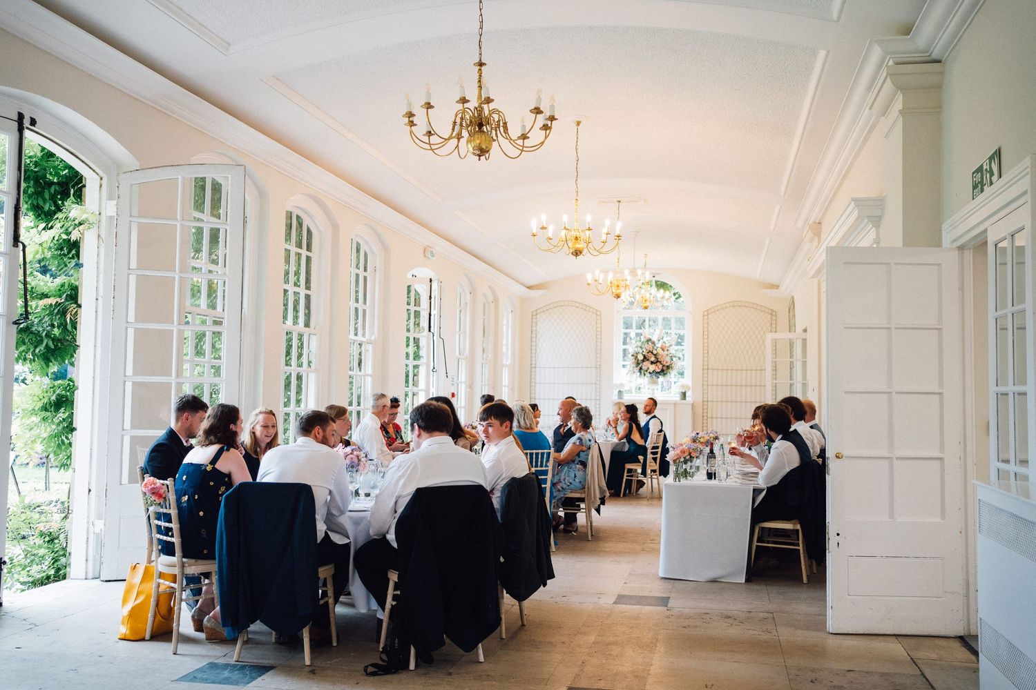 Panoramic view of an elegant white wedding reception hall with chandeliers and large windows.