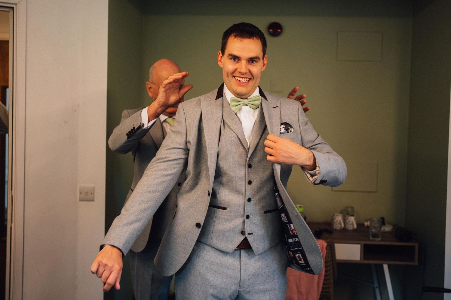 Groomsmen in matching gray suits joke around during wedding day preparations.