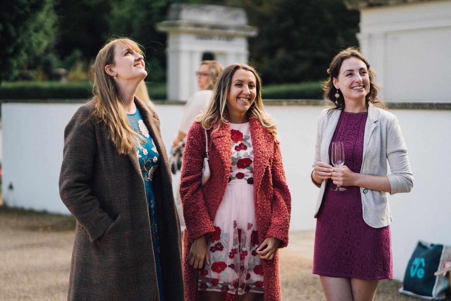 Wedding party members stand in casual conversation outside a historic stone building.