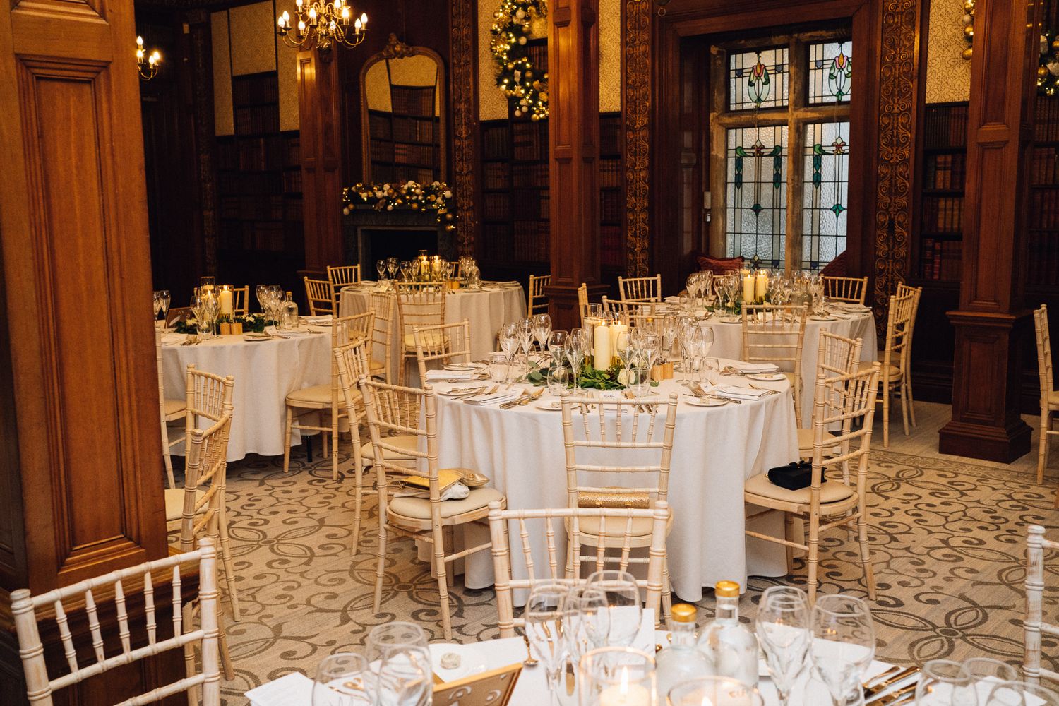 Elegant wedding reception hall with round tables, gold chiavari chairs, white linens, and candlelit centerpieces.