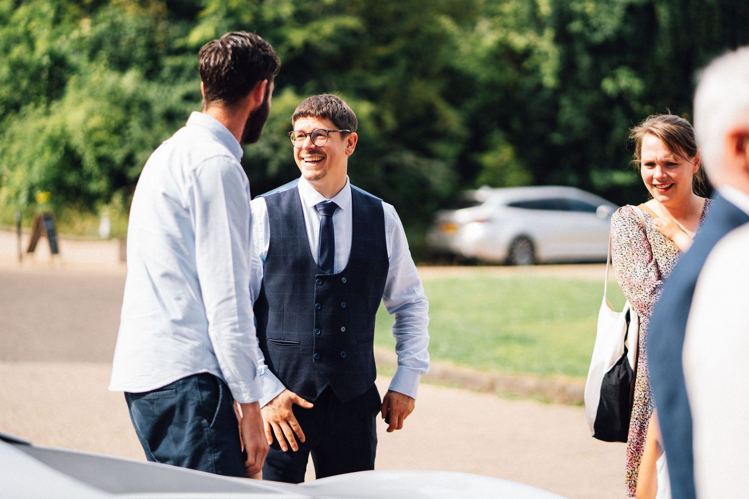 Wedding guests mingle and socialize during an outdoor reception on a sunny day.