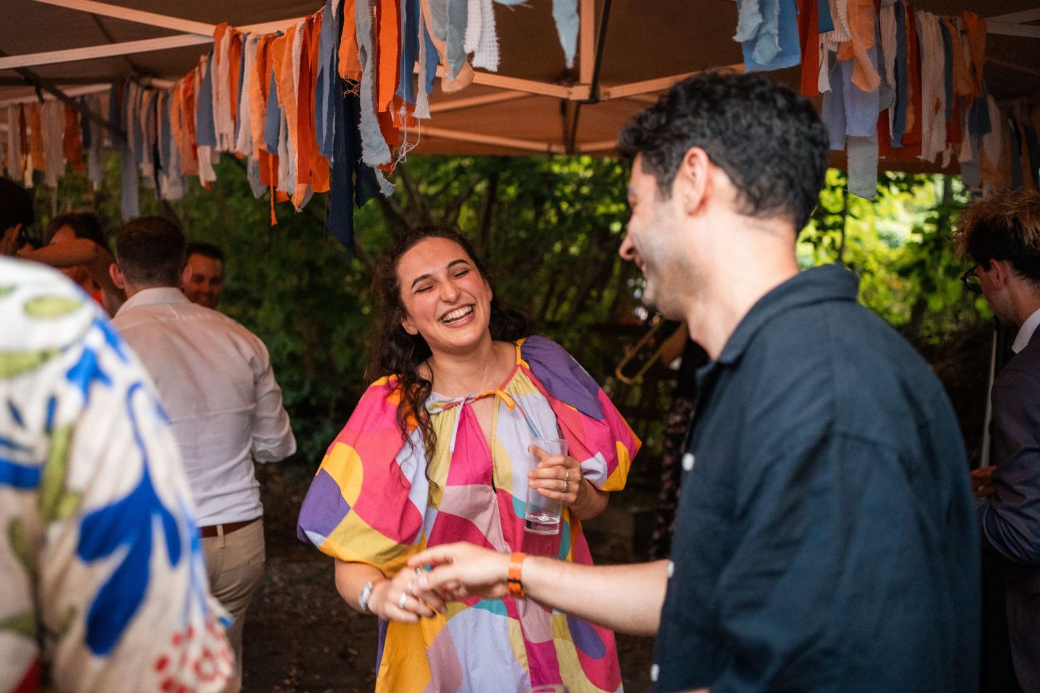 Woman in colorful dress laughs with guest at outdoor wedding reception party.