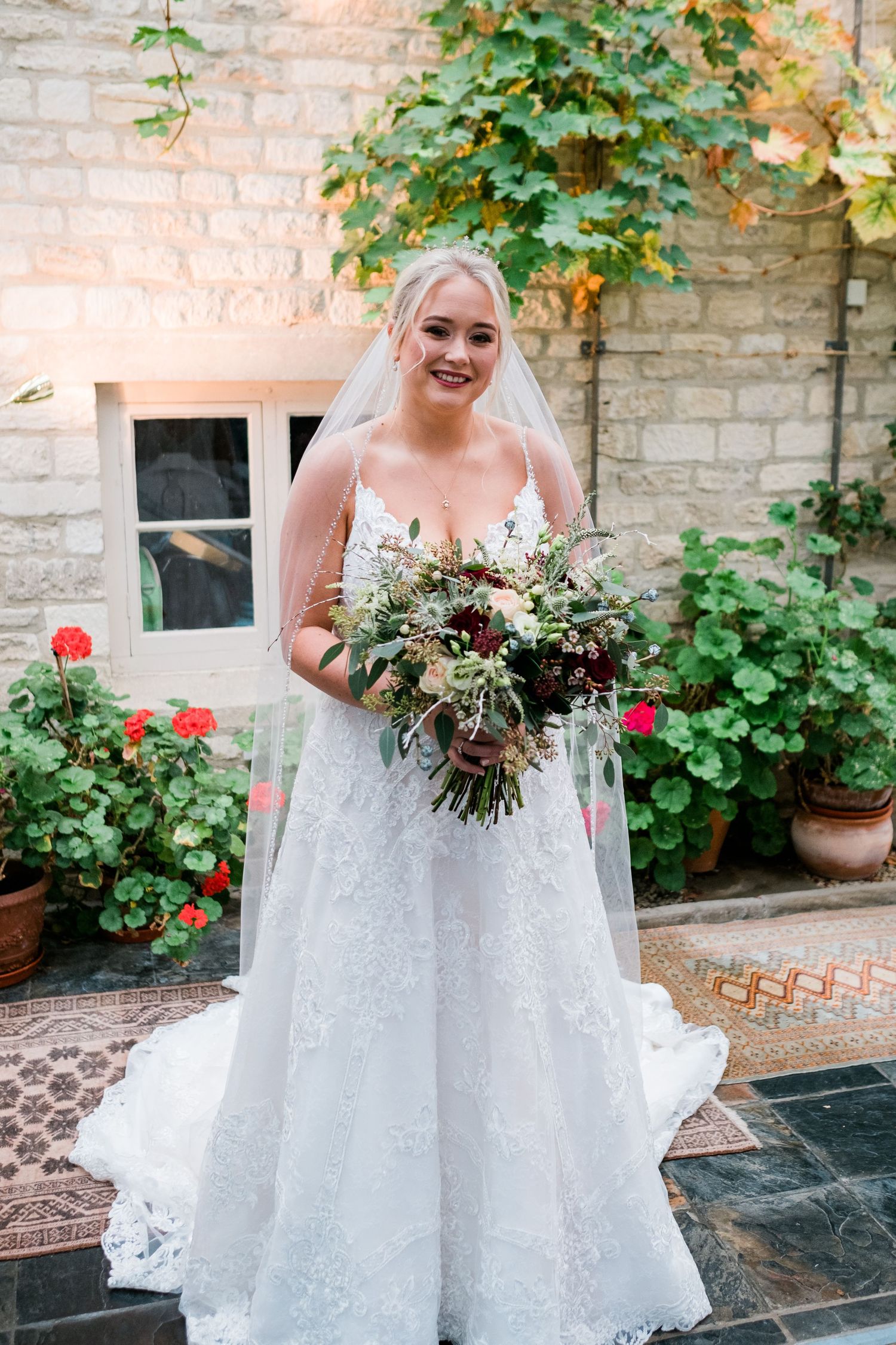 Beautiful bridal moment with a lush bouquet against a stone wall backdrop with climbing roses.