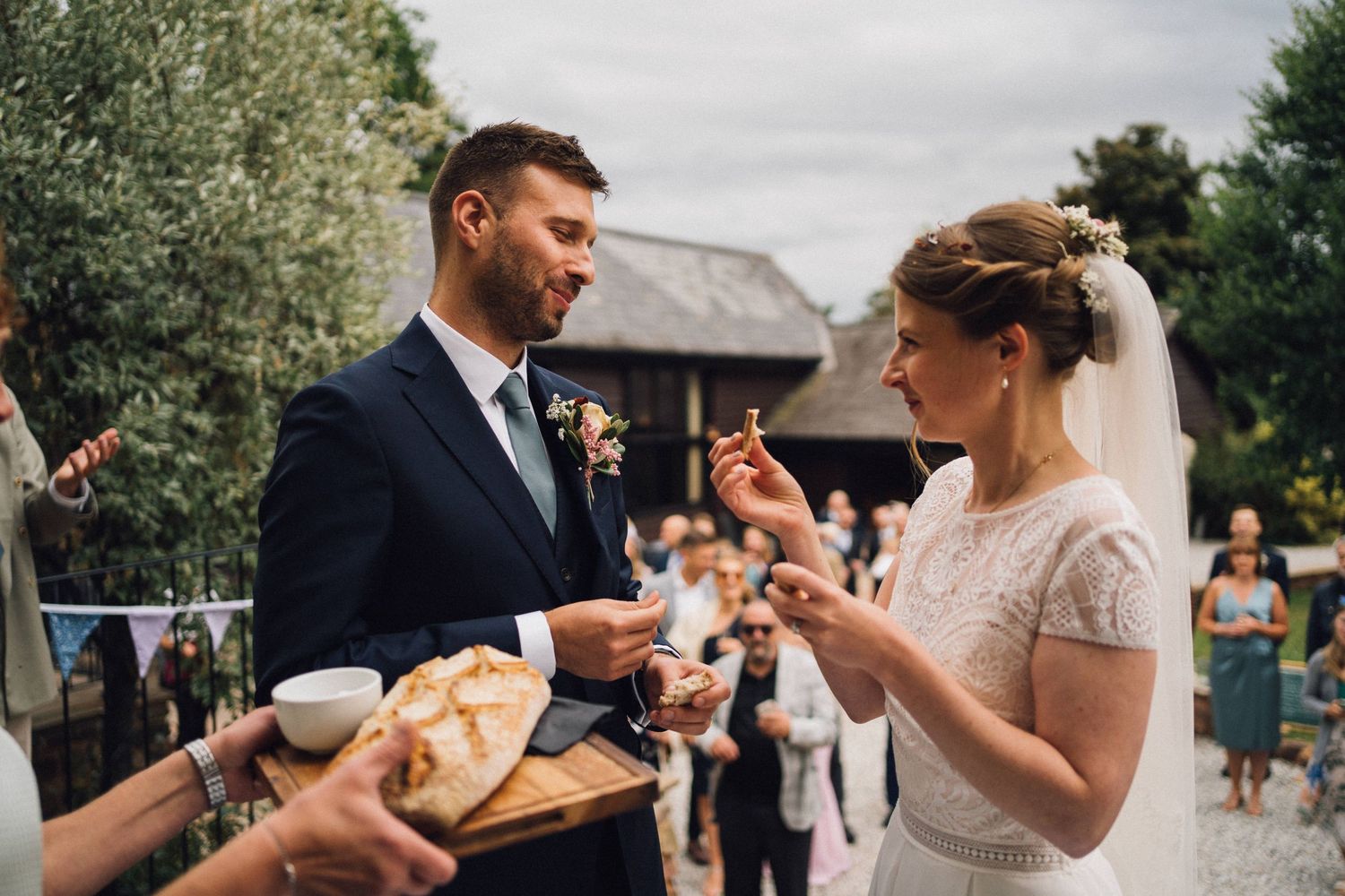 Newlyweds participate in a traditional bread sharing ritual outdoors.
