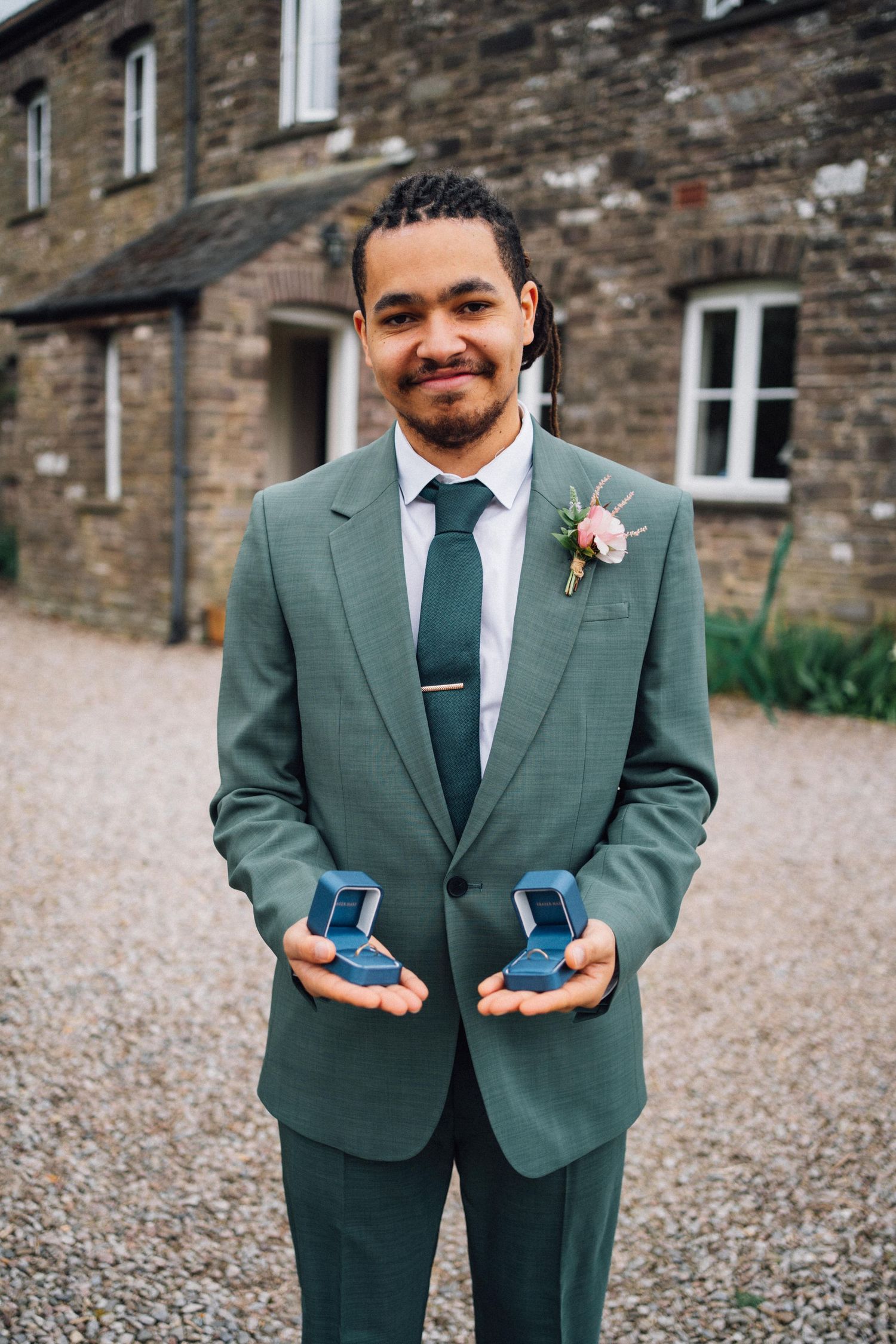 A person in a green suit jacket holds two blue items while smiling at the camera.
